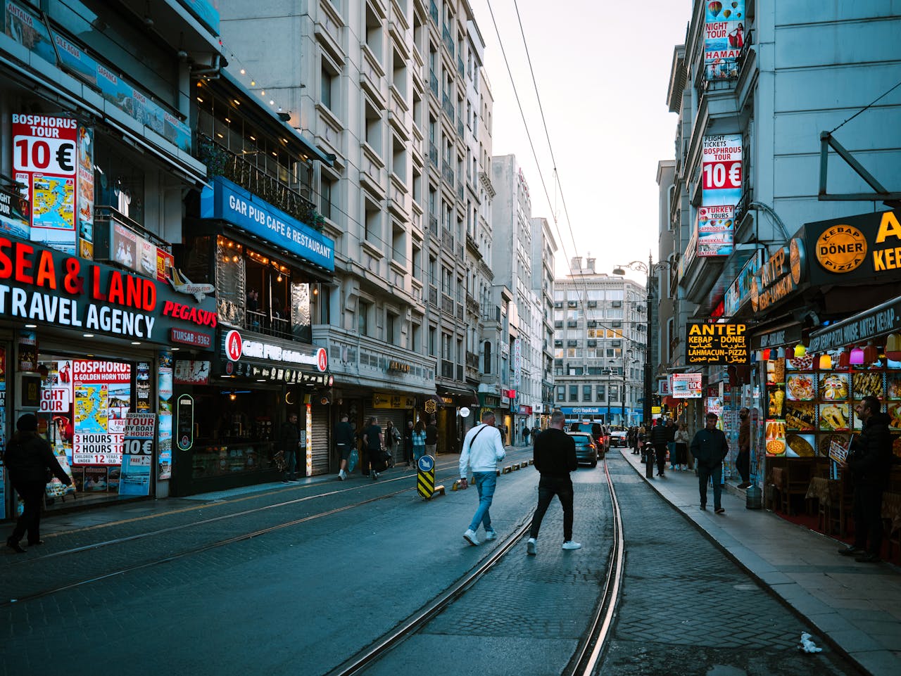 Vibrant street scene in Istanbul featuring shops, people, and tram tracks under a clear sky.